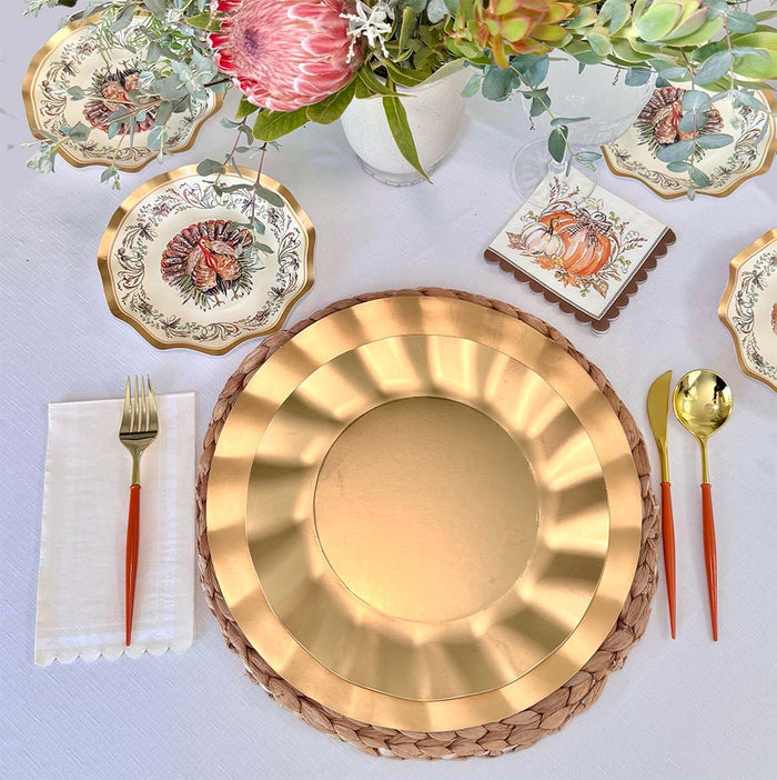 Create a stunning Thanksgiving table with the Sophistiplate Turkey & Gourds Table Setting, featuring designer paper plates, a gold charger, woven placemat, orange-handled flatware, white napkin, and floral centerpiece.