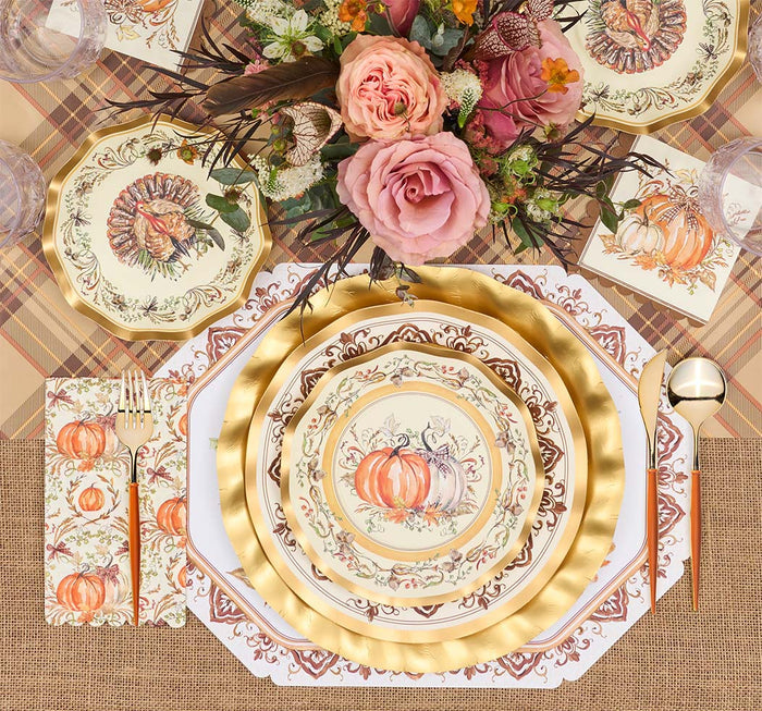 A fall-themed table setting features the Turkey & Gourds Table Setting Bundle by Sophistiplate LLC, including designer disposable plates adorned with turkey and gourd motifs, gold cutlery, plaid and burlap placemats, and a floral centerpiece with pink roses and autumnal blooms. The distinctive turkey design appears on both the top plate and matching napkin.