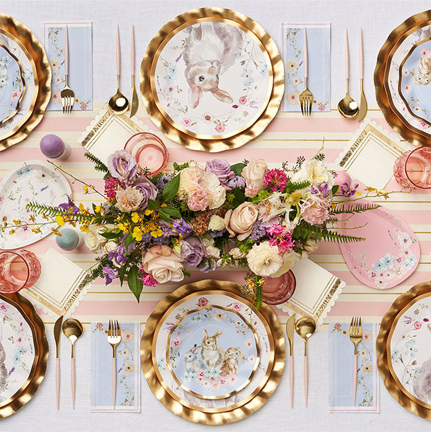 Create a festive Easter table for 16 with Sophistiplate LLC’s Ultimate Easter Tablescape: charming bunny plates, gold cutlery, floral napkins, pink glassware, and a spring centerpiece accented by decorated eggs.