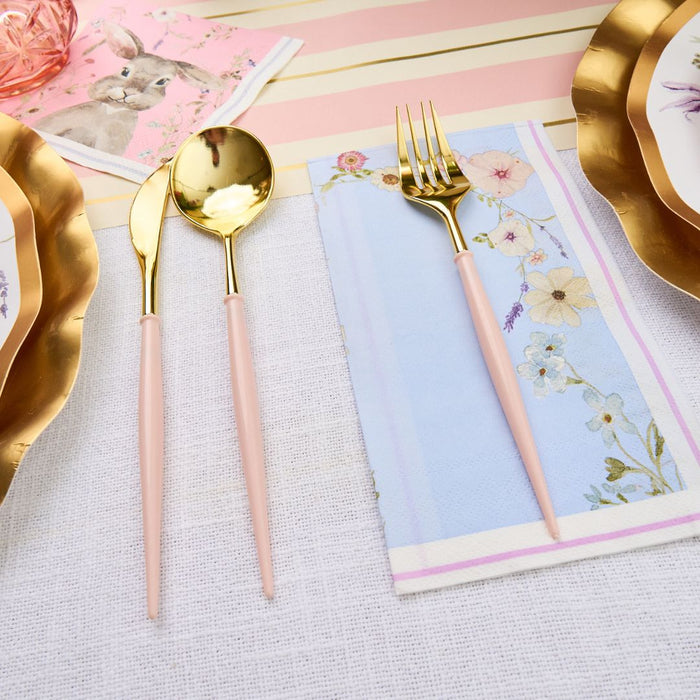 The Ultimate Easter Tablescape for 16 by Sophistiplate LLC features scalloped gold designer paper plates, pink and gold cutlery, floral napkins, and pink rabbit illustration napkins on a white tablecloth with pastel stripes—perfect for charming celebrations.