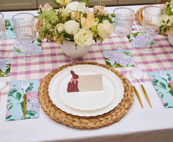 Create a spring-inspired table with the Ultimate Easter Tablescape for 16: Violet Hydrangea by Sophistiplate LLC, featuring floral plates, gold cutlery, glassware, napkins, and bunny place cards for a charming holiday centerpiece.
