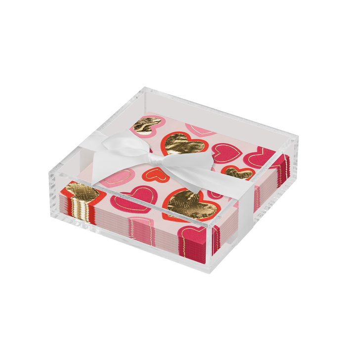 The Sophistiplate Valentines Day Cocktail Napkin with Napkin Tray holds heart-printed napkins in pink, red, and gold, tied with a white ribbon—an elegant touch to any modern tabletop.