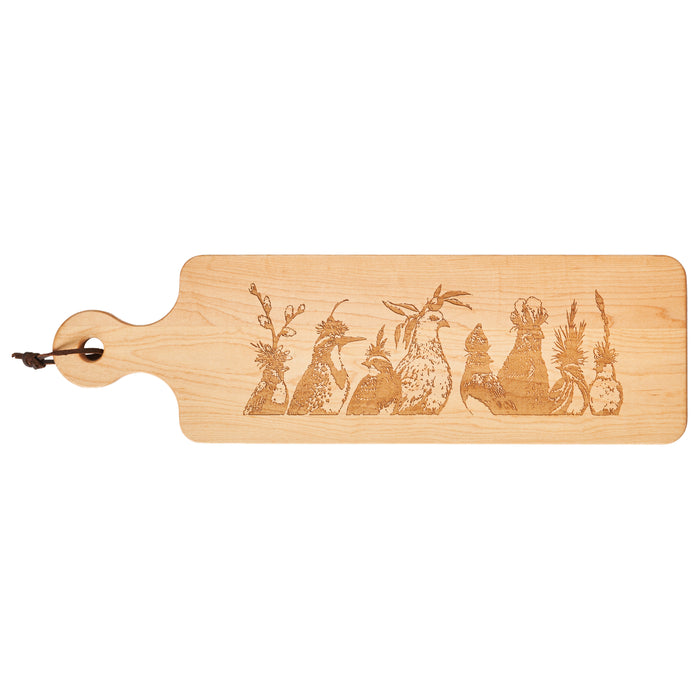 The Maple Vicki Sawyer "Peace Was The Central Theme" Maple Wood Cheeseboard, 20 x 6", features six engraved chickens in quirky poses and includes a handle with a leather loop. Made in the USA.