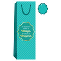 The Vineyard-Wine Bag by Drinks On Me features teal stripes, a gold-edged label reading "It doesn’t take a Village, it takes a Vineyard," and comes with a matching teal gift tag—ideal as a fun hostess gift.