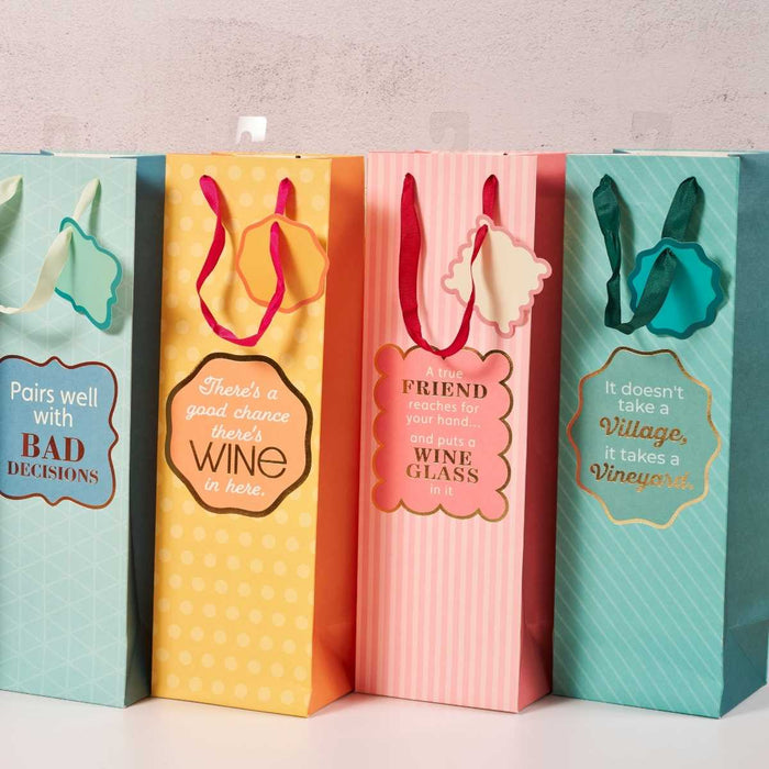 Four Vineyard-Wine Bags by Drinks On Me stand in a row, each with a unique wine-themed message, matching ribbon handles, and tags—funny, reusable gifts for any hostess. Set against a plain, light-colored background.