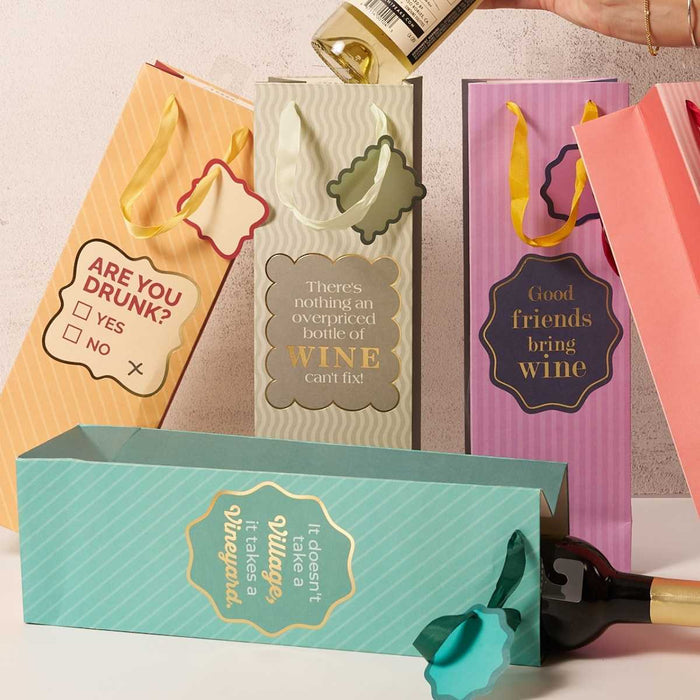 Drinks On Me's Vineyard-Wine Bag set features four colorful, reusable wine bags with witty wine quotes, playful designs, and yellow ribbon handles—perfect hostess gifts for any wine lover.