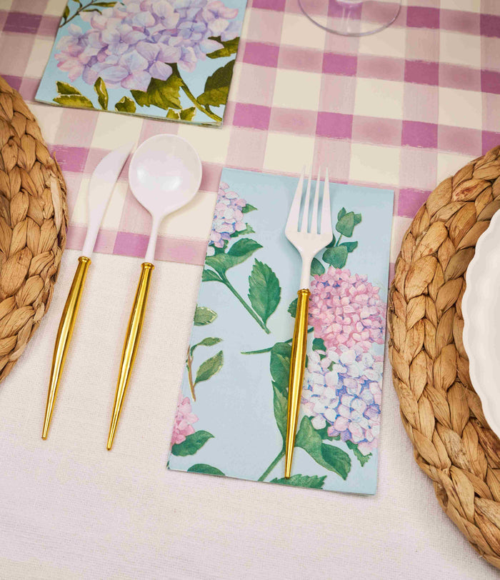 The Ultimate Easter Tablescape for 16: Violet Hydrangea by Sophistiplate LLC features a pink and white checkered tablecloth, floral napkins, gold-handled cutlery, designer disposable plates on woven placemats, and white plastic utensils.