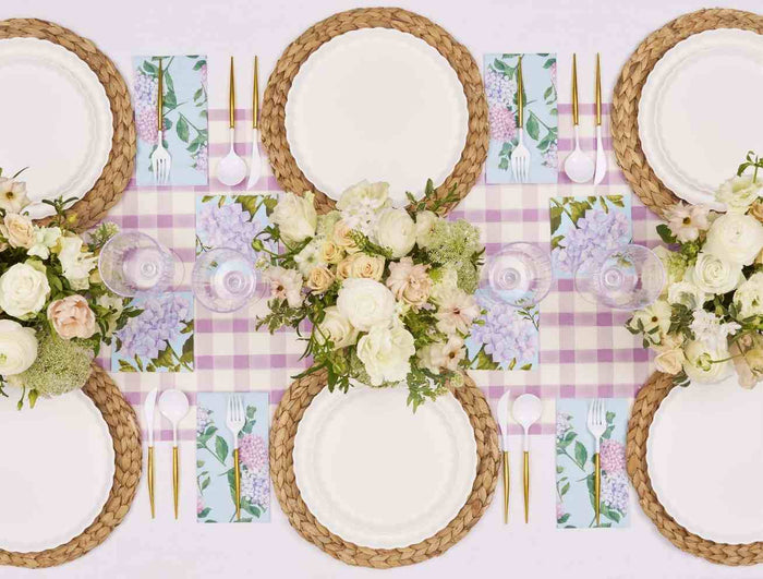 Create a spring look with the Ultimate Easter Tablescape for 16: Violet Hydrangea by Sophistiplate LLC, featuring woven placemats, floral plates, gold cutlery, and pink gingham touches for a designer table setting.