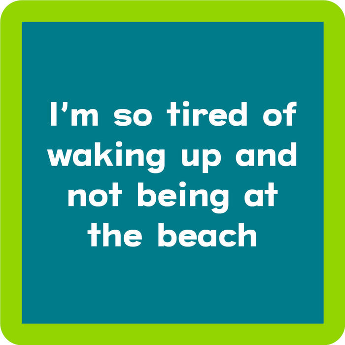 Text graphic on the Waking Up Coaster by Drinks On Me features white text—"I’m so tired of waking up and not being at the beach"—on a blue background with a light green border. Perfect for funny drink coasters or unique housewarming gifts.