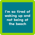 Text graphic on the Waking Up Coaster by Drinks On Me features white text—"I’m so tired of waking up and not being at the beach"—on a blue background with a light green border. Perfect for funny drink coasters or unique housewarming gifts.