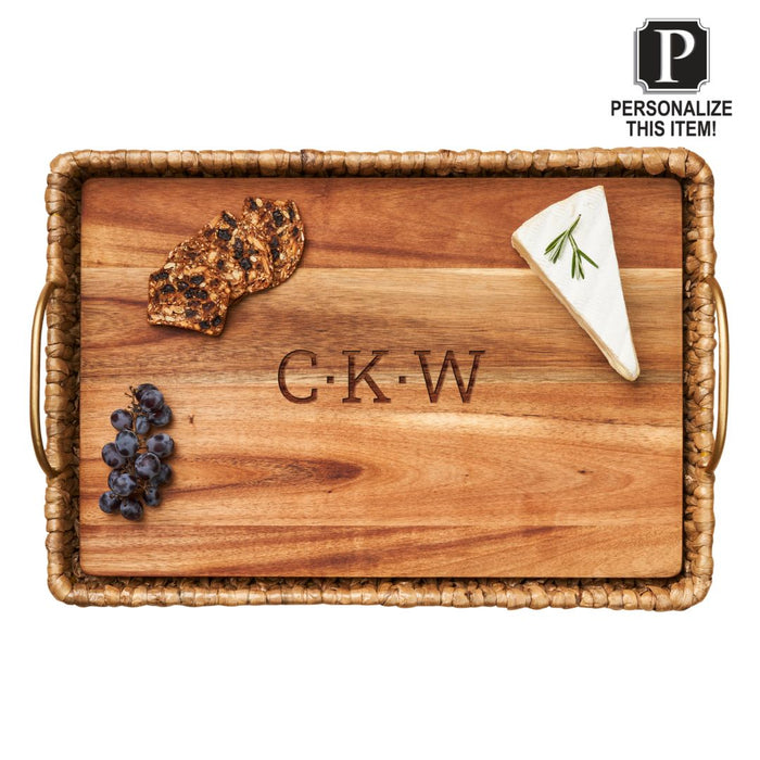 The Maple Water Hyacinth Rectangle Tray with Metal Handles and a personalized Acacia wood liner (19.5 x 13.5 x 4.5”) elegantly serves crackers, cheese with rosemary, and grapes, featuring engraved initials "C-K-W" at the center.