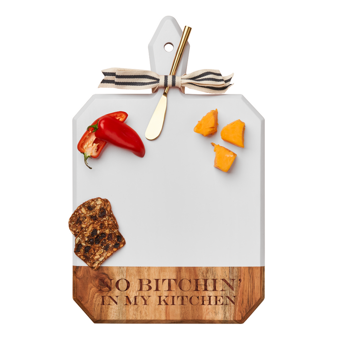 The Maple Acacia Heirloom Board Rectangle in white (16x10") is engraved with "No Bitchin In My Kitchen" and comes topped with a gold spreader, ribbon, cheese, red pepper, and crackers.