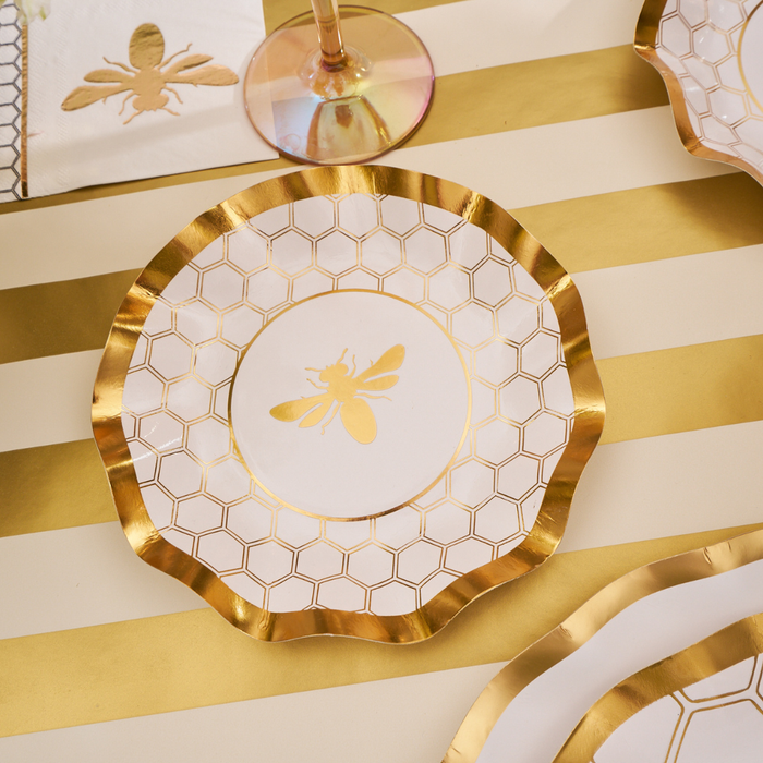 A set of White Honeybee Appetizer/Dessert Bowls from Sophistiplate, featuring elegant honeycomb and bee motifs, is arranged on a striped gold and white tablecloth alongside coordinating napkins and glassware.