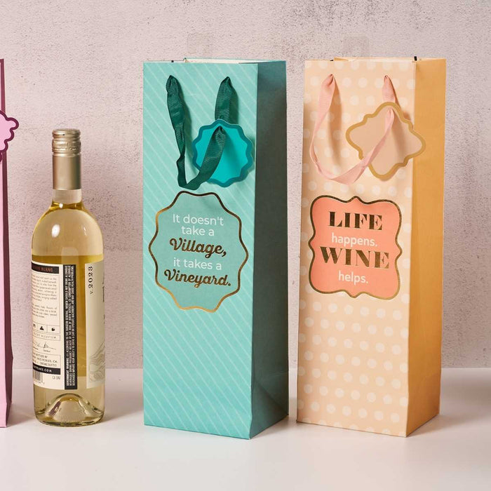 The Drinks On Me "Wine Helps" wine bag features playful peach polka dots and the saying "Life happens. Wine helps."—a perfect reusable gift for hosts. A bottle of white wine completes the set.