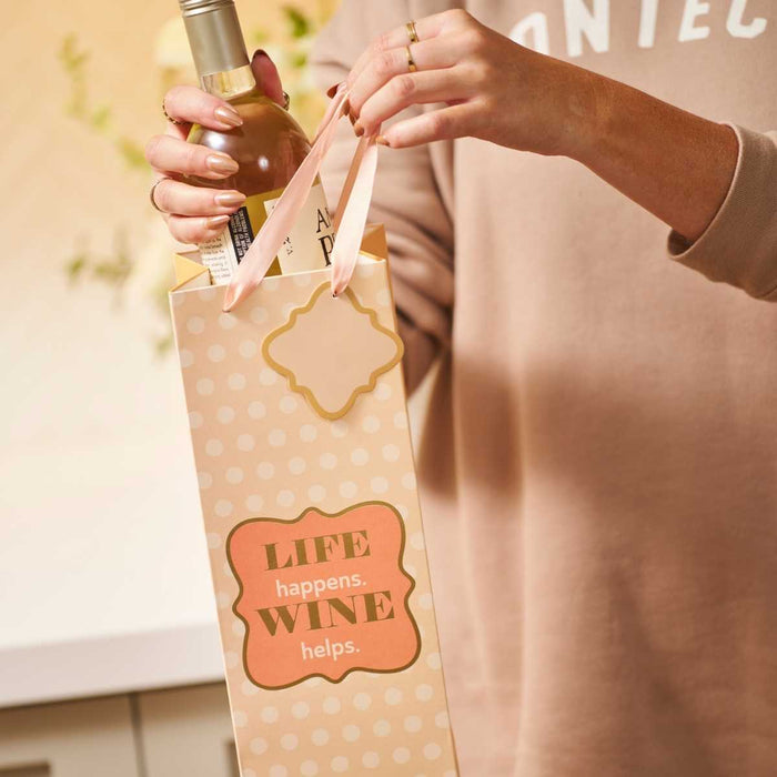 A person puts white wine into the Drinks On Me "Wine Helps" wine bag featuring polka dots and a LIFE happens. WINE helps label—an ideal hostess gift that adds humor to any occasion.