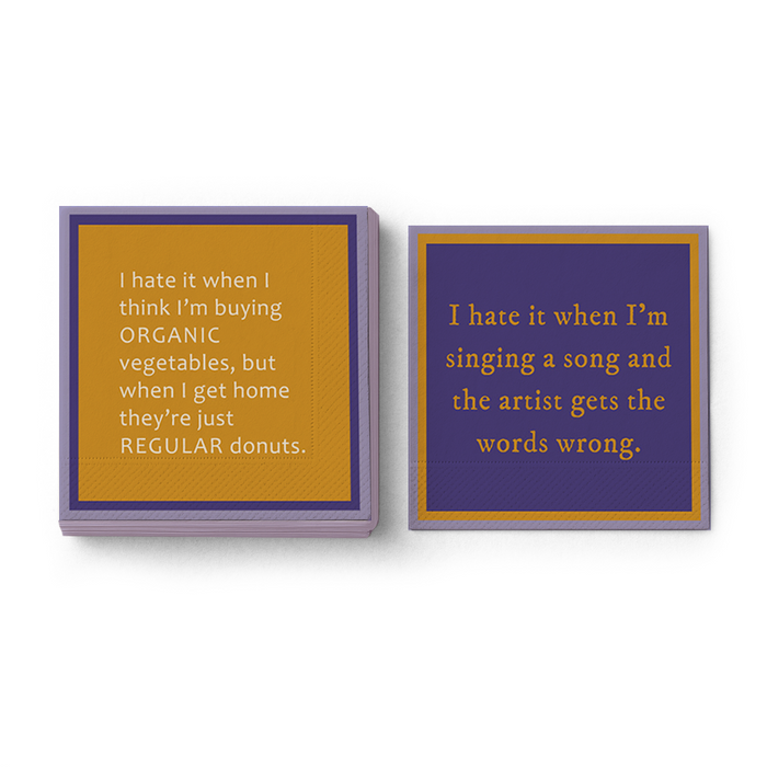 The Drinks On Me Words Wrong Napkin set includes a mustard napkin with witty organic vegetable text and a purple one with gold song lyrics—funny complaints perfect for quirky birthday parties or as playful bar cart accessories.