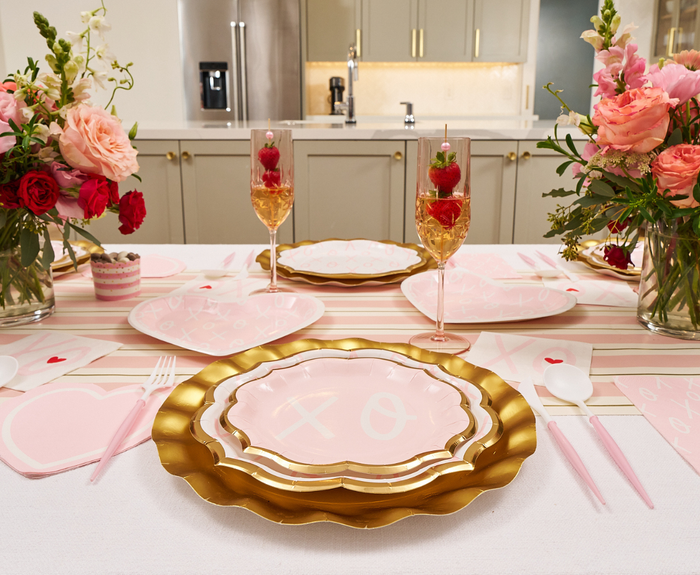 A modern kitchen set for a celebration with Sugarplum XOXO Salad Plates (8pk), gold accents, heart-shaped placemats, floral centerpieces, and champagne glasses with raspberries.