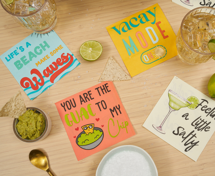 Sugarplum’s Vacay Mode On Cocktail Napkins (26pk), tortilla chips, guacamole, a lime, iced drinks, and salt are arranged on a bamboo surface for a fun summer vibe.